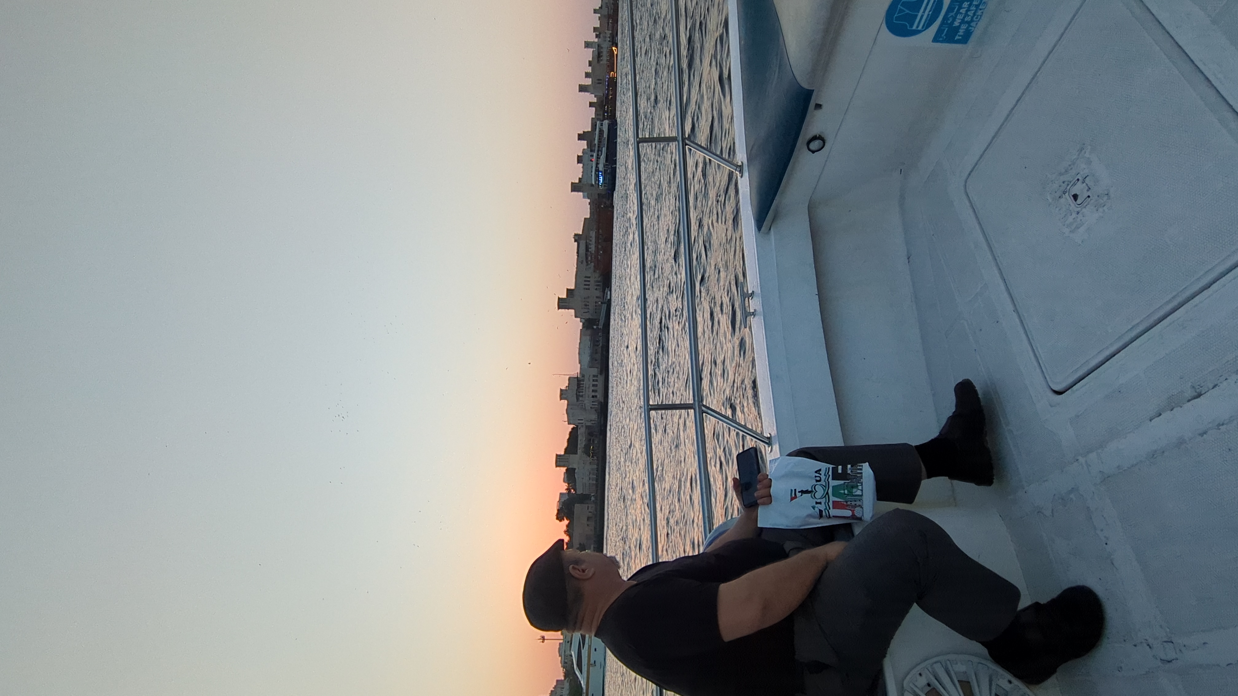 Un homme assis sur un bateau regarde la rive au coucher du soleil.