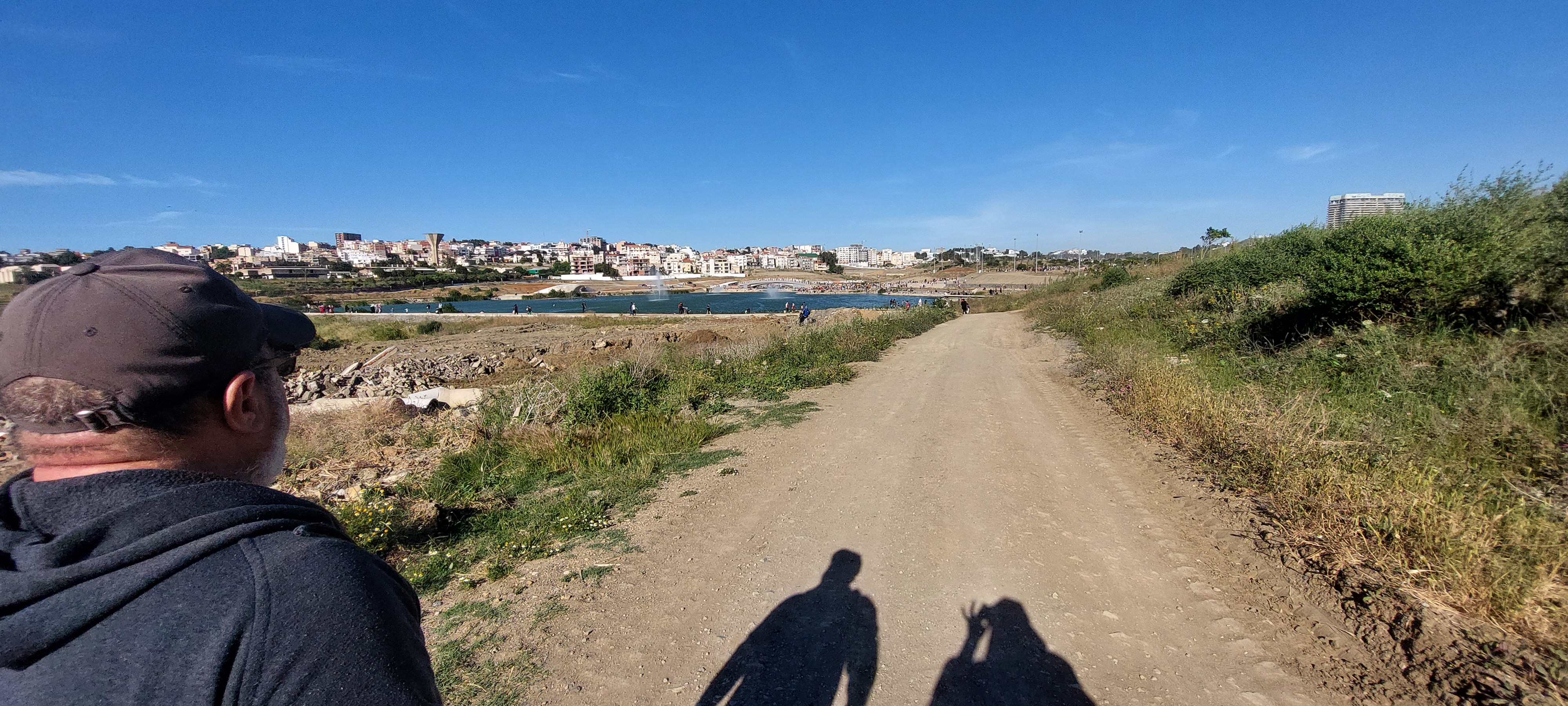 Un homme et deux ombres sur un chemin ensoleillé au bord de la mer.